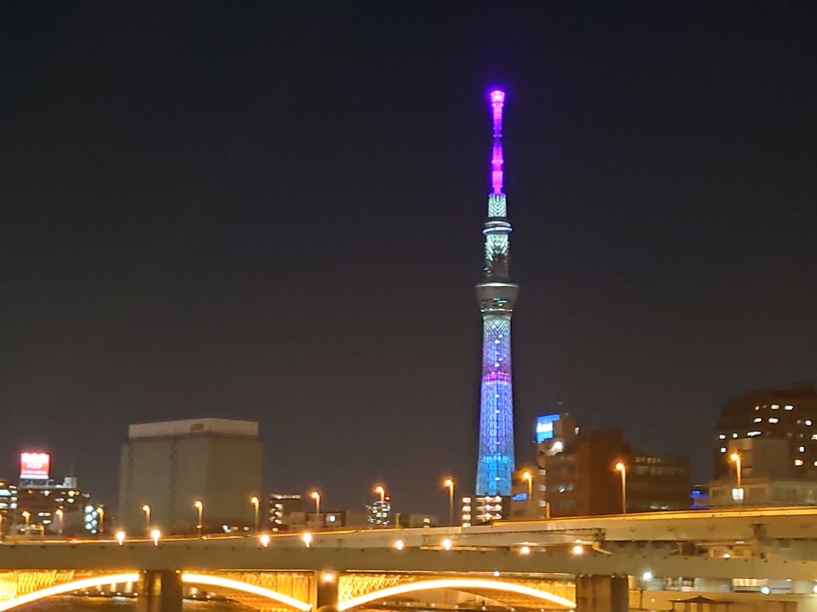 Tokyo Skytree lit at night above the Sumida River, seen from the Sumida side of the water